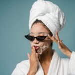 black female with sheet mask in sunglasses and towel on head